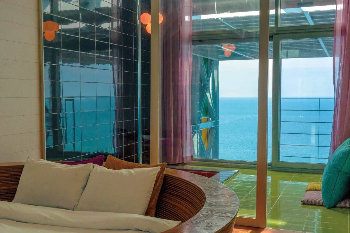 Une chambre moderne avec un lit en bois aux lignes courbes, un mur en verre et une vue sur la mer.