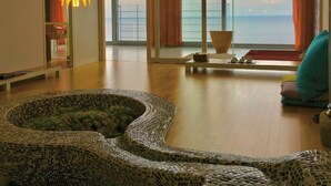 Een moderne woonkamer met een groot raam, een mozaïek vloerkleed en uitzicht op zee.