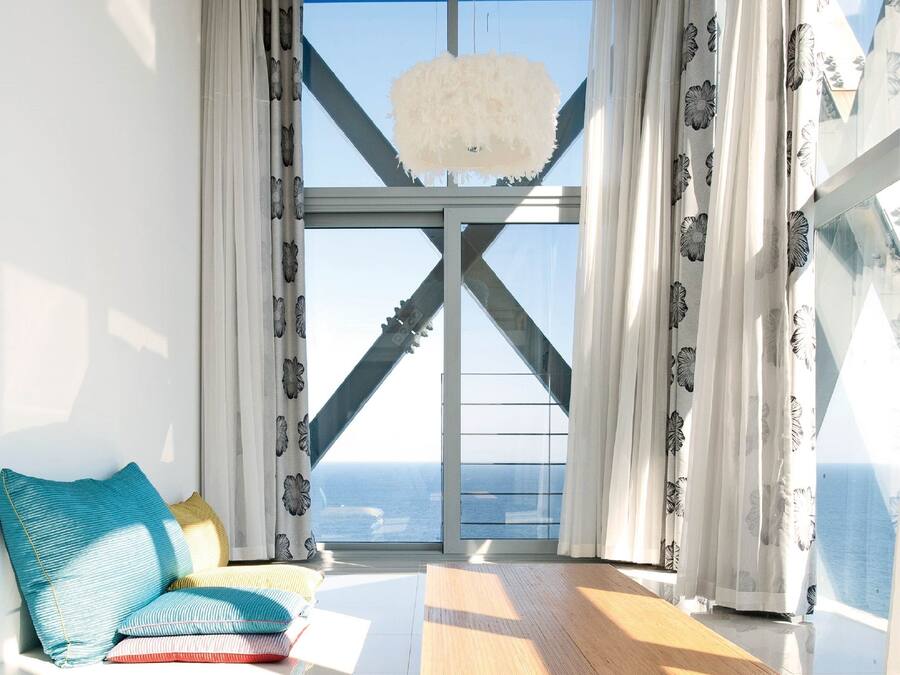 Ein Zimmer mit großem Fenster, Deckenventilator in Weiß und Blick auf den Ozean.