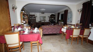 A dining area with a red tablecloth, wooden chairs, and a patterned tablecloth. There is a bookshelf in the background and a chandelier above the dining table. - Fortview House Bed & Breakfast (Belturbet)