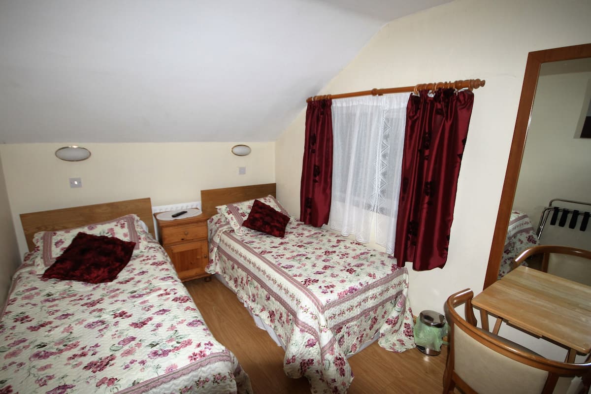 Ein Schlafzimmer mit zwei Einzelbetten, einem hölzernen Nachttisch, einem kleinen Tisch und einem Spiegel.