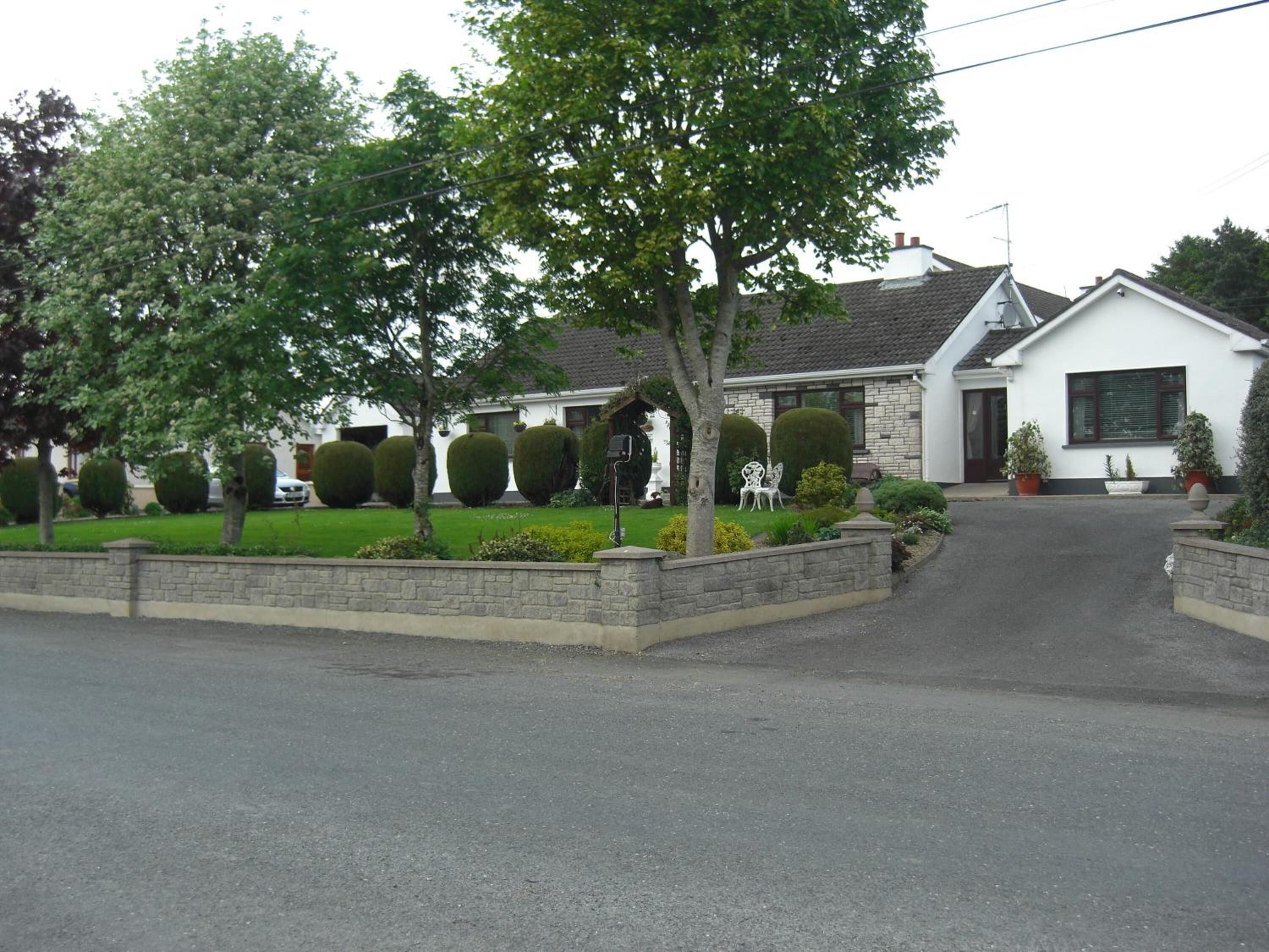 A residential house with a paved driveway, neatly trimmed hedges, and a well-maintained lawn.