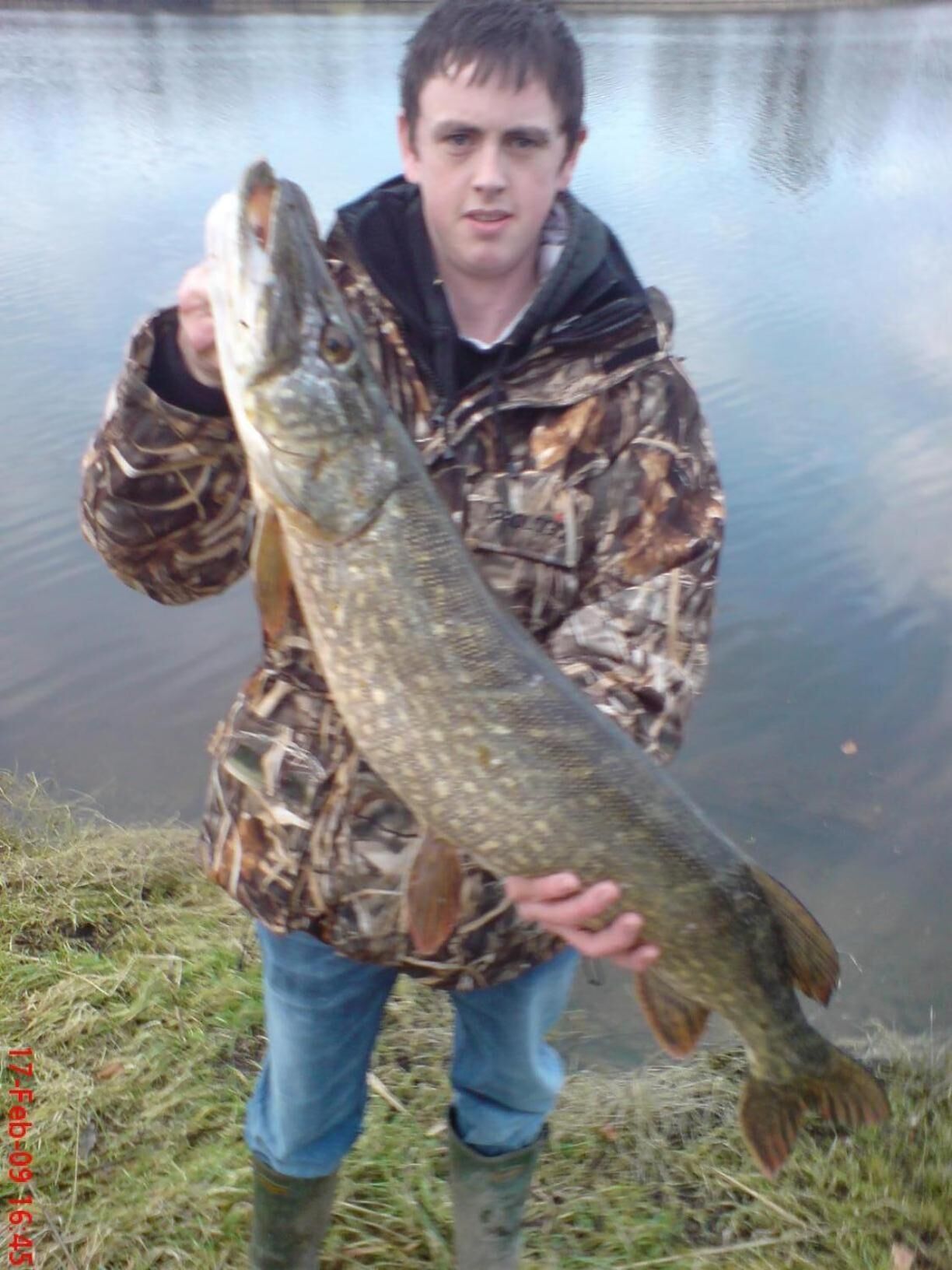 A person holding a large fish by a body of water.
