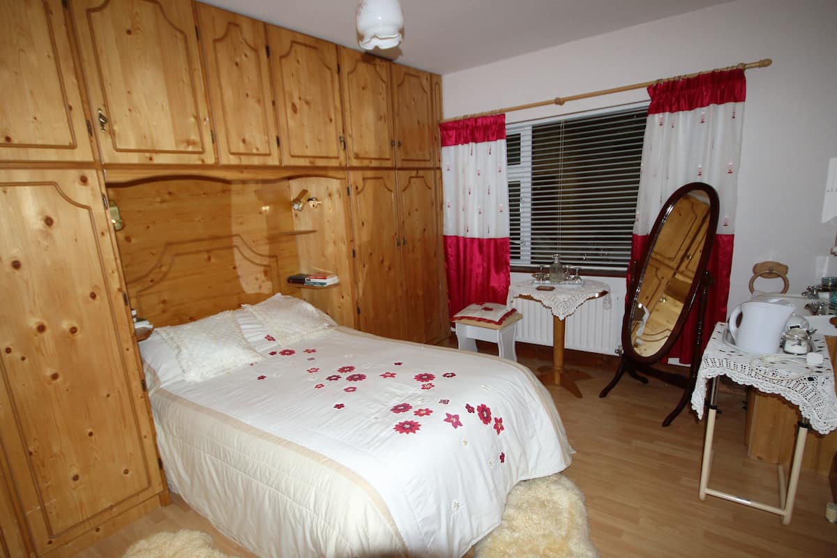 Ein Schlafzimmer mit einem Holzschrank, einem Bett mit floralem Bettzeug, einem kleinen Tisch mit Spitzenbettdecke und einem Spiegel.