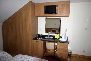 Un dormitorio con un armario de madera, un escritorio con silla, un televisor y un espejo.