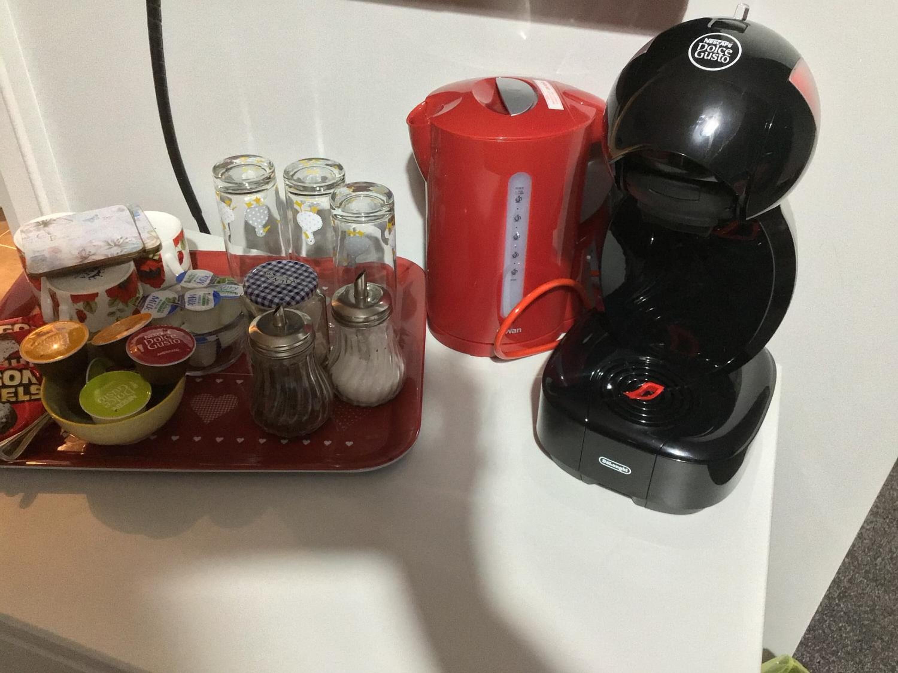 A kitchen counter with a coffee maker, a red kettle, and various condiments and jars.