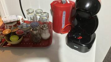 A kitchen counter with a coffee maker, a red kettle, and various condiments and jars.