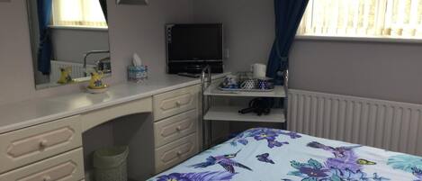 A bedroom with a bed, dresser, vanity, and a television.