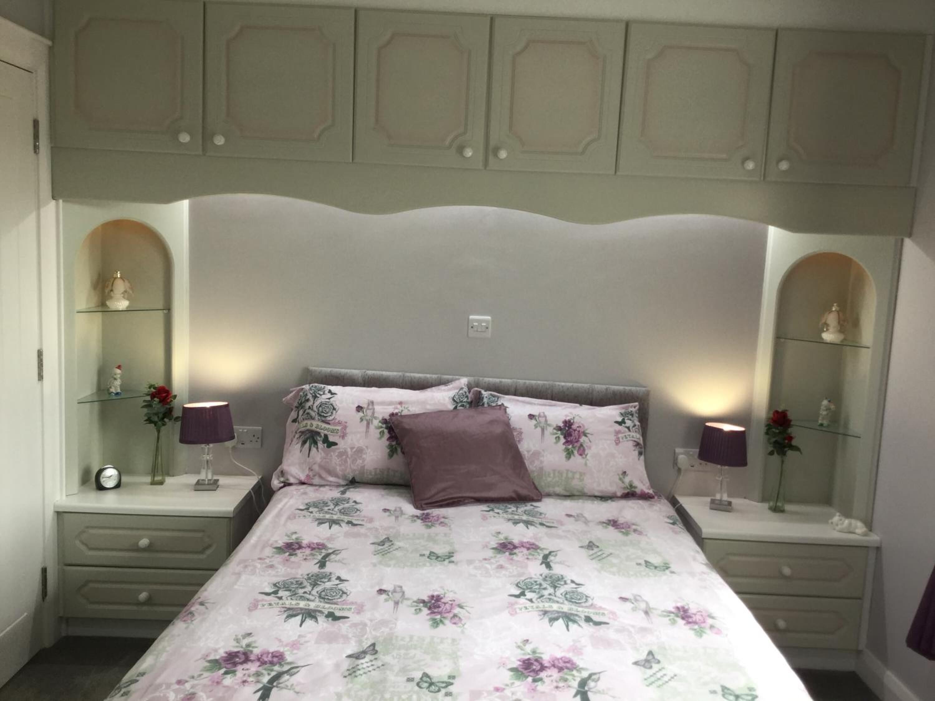 Een slaapkamer met een bloemenbedekking, een hoofdeinde, nachtkastjes met lampen en decoratieve objecten.
