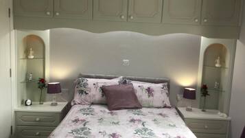 Een slaapkamer met een bloemenbedekking, een hoofdeinde, nachtkastjes met lampen en decoratieve objecten.