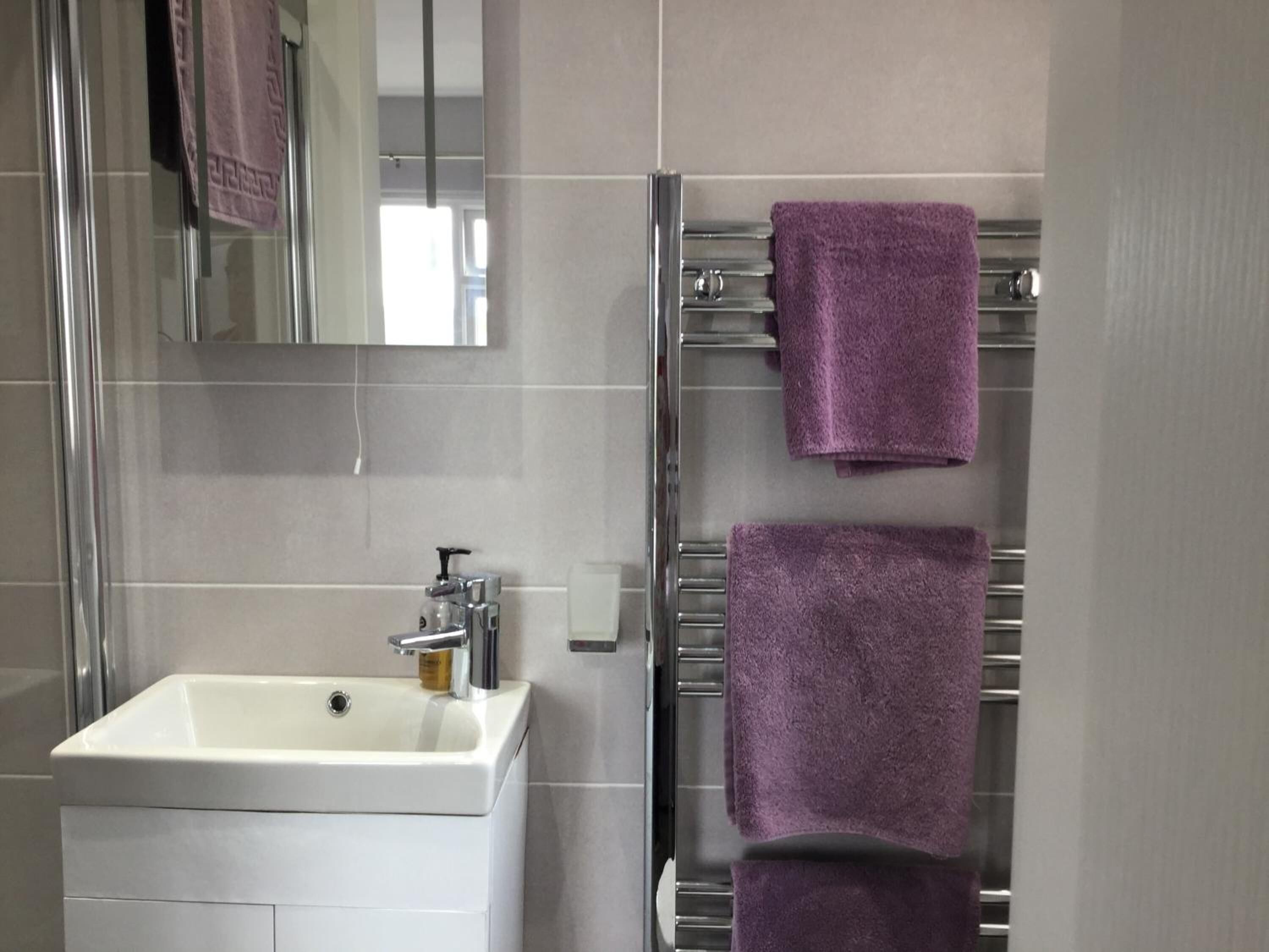 Une salle de bain avec un lavabo blanc, un miroir et deux serviettes violettes sur un porte-serviettes.