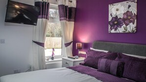 A bedroom with a bed, a nightstand, a lamp, a TV, and a window with curtains. - Garron View Bed and Breakfast (Ballymena)