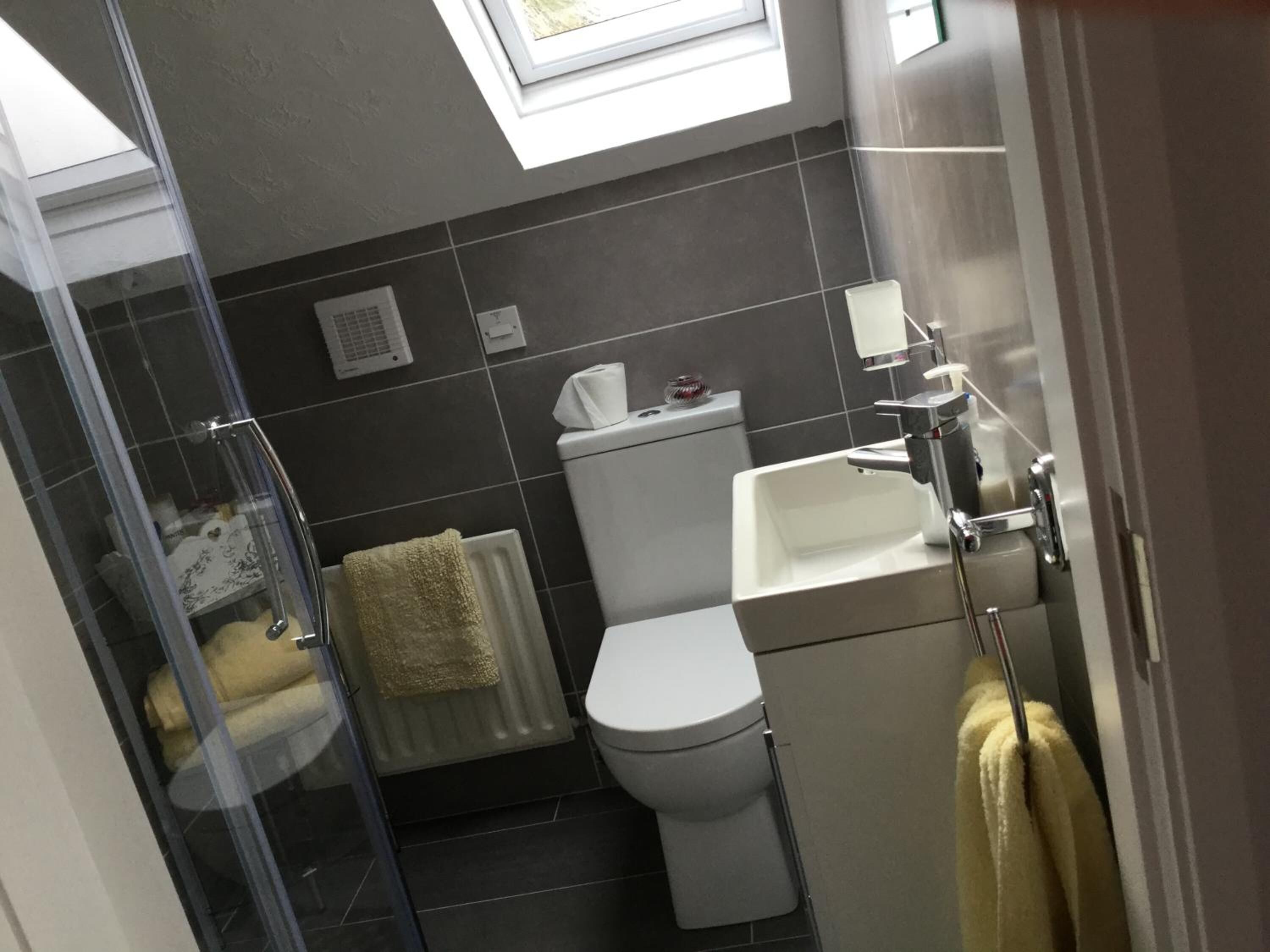 A bathroom with a toilet, sink, and shower. There is a towel rack and a radiator.