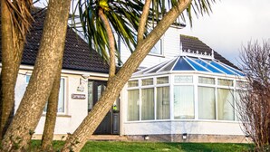 A house with a conservatory, a door with a sign, and a well-maintained lawn. - Garron View Bed and Breakfast (Ballymena)
