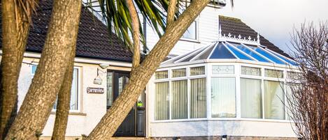 A house with a conservatory, a door with a sign, and a well-maintained lawn.