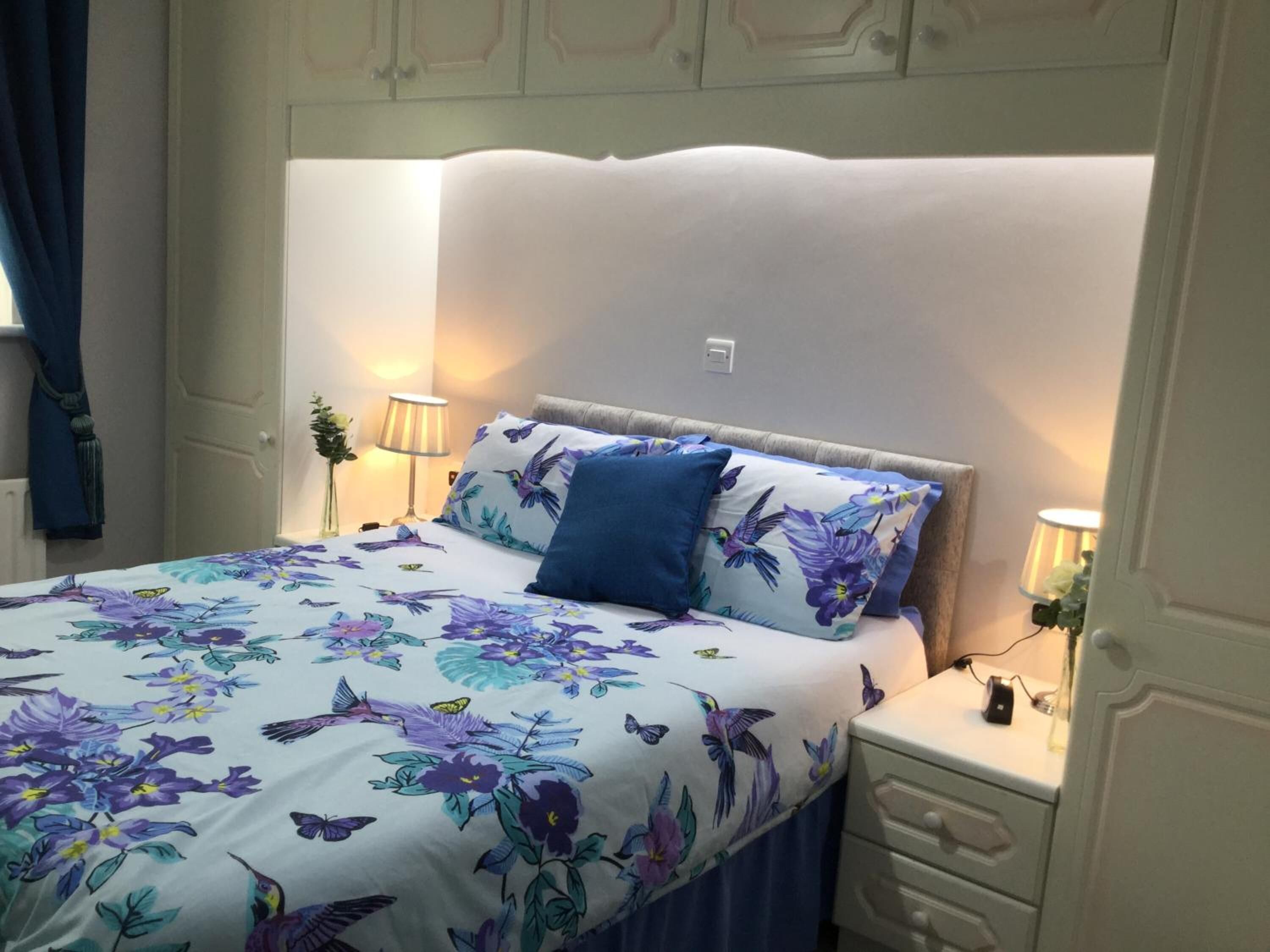 A neatly made bed with floral bedding, two bedside lamps, and a nightstand with a lamp.