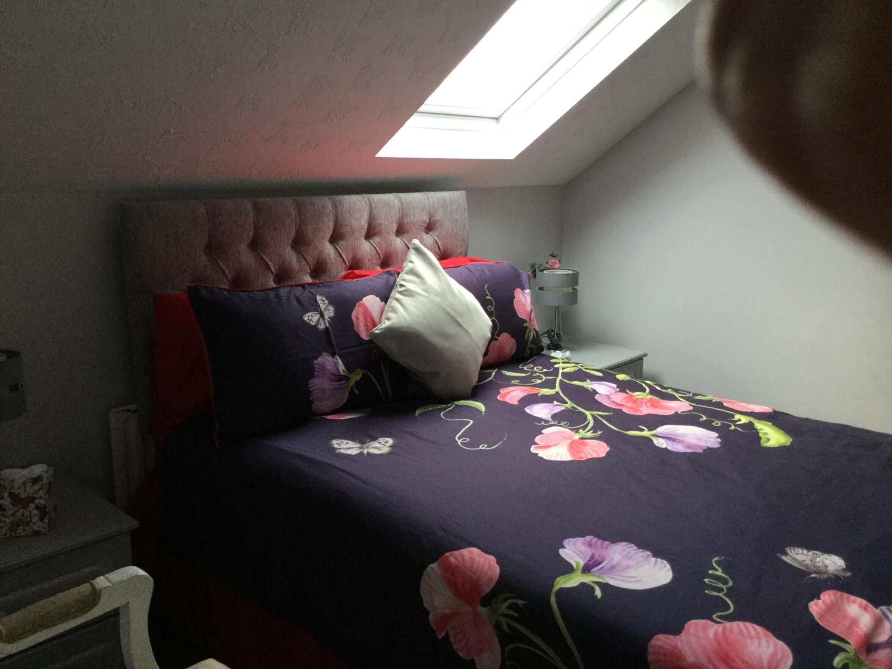 A bedroom with a tufted headboard, a floral bedspread, and a skylight.