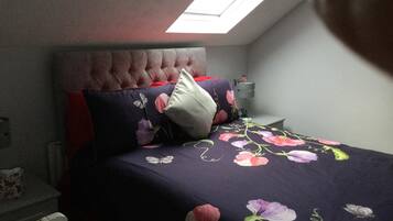 A bedroom with a tufted headboard, a floral bedspread, and a skylight.