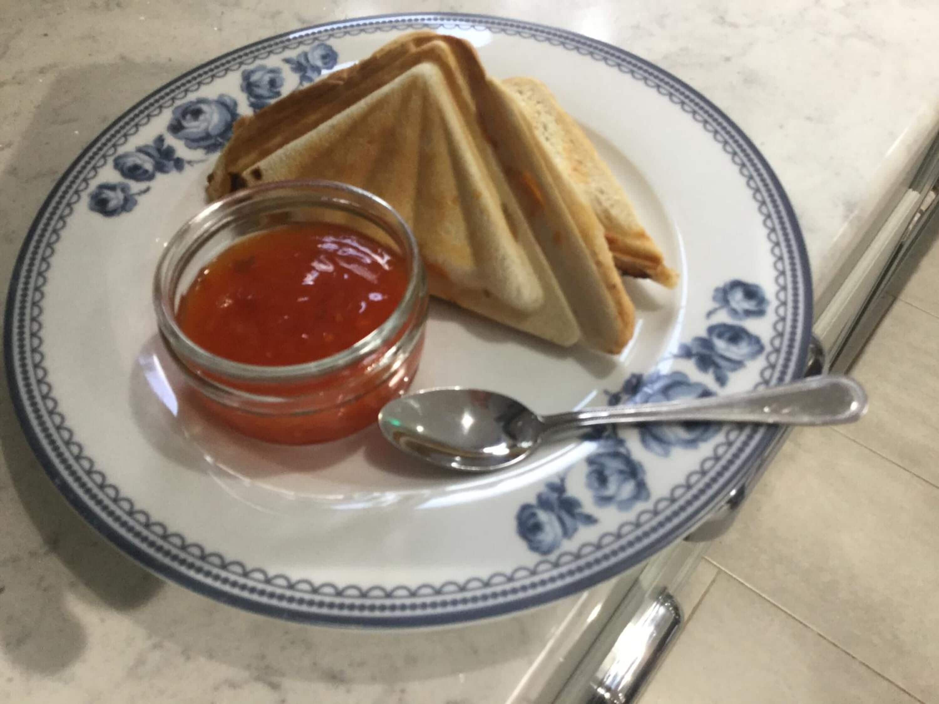 Une assiette avec un sandwich et un petit pot de sauce, accompagnée d’une cuillère.