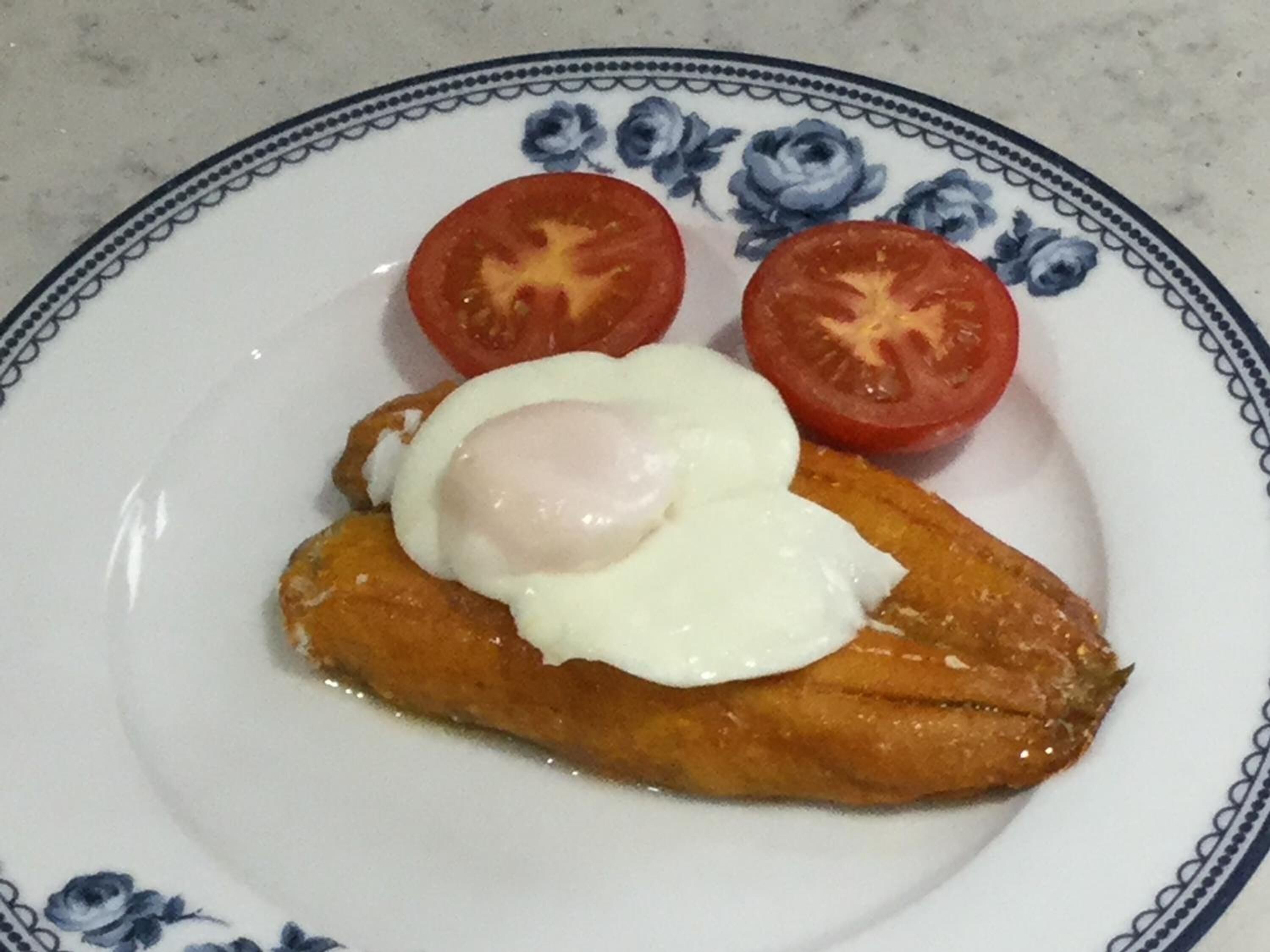 A plate with a fried egg, two slices of tomato, and a piece of bread.