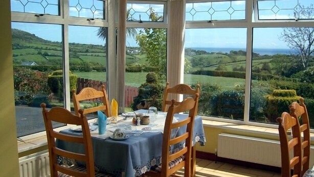 A conservatory with a table set for two, overlooking a scenic landscape. - Garron View Bed and Breakfast (Ballymena)