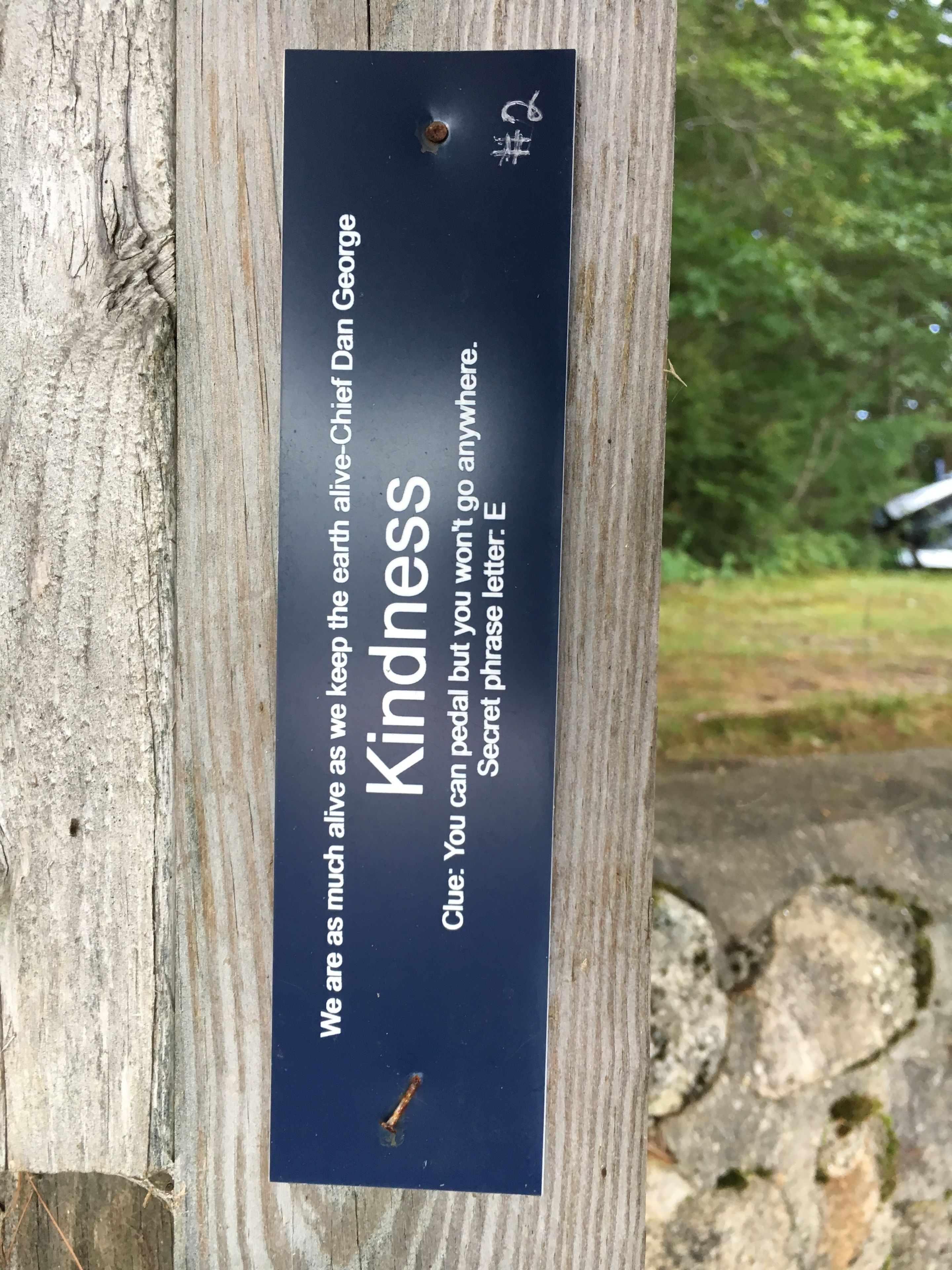 Un poteau en bois sur lequel est fixée une plaque noire portant les inscriptions « Gentillesse » et « Nous sommes aussi vivants que la Terre que nous préservons – Chef Dan George. »