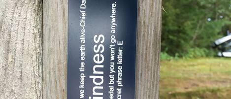 A wooden post with a black plaque that reads "Kindness" and "We are as much alive as we keep the earth alive - Chief Dan George."
