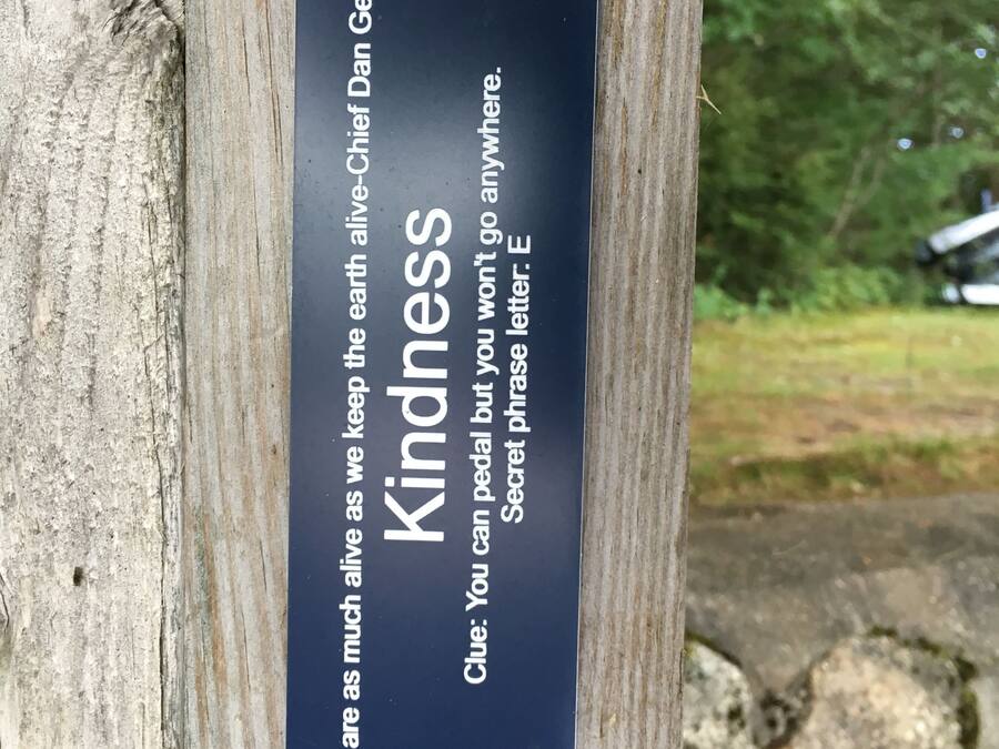 Un poteau en bois sur lequel est fixée une plaque noire portant les inscriptions « Gentillesse » et « Nous sommes aussi vivants que la Terre que nous préservons – Chef Dan George. »
