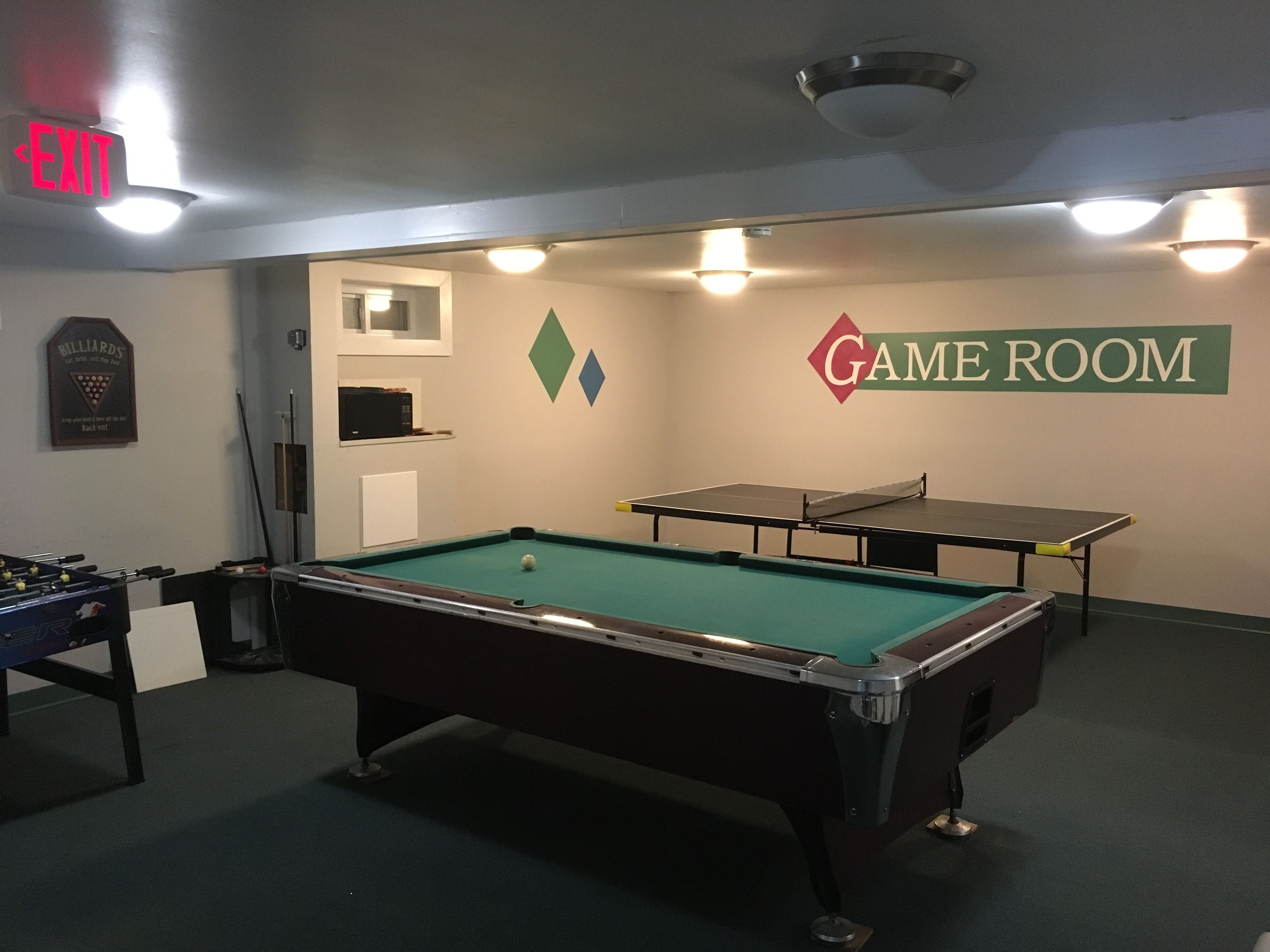 A pool table in a room with a billiards sign, a foosball table, and a table tennis table.