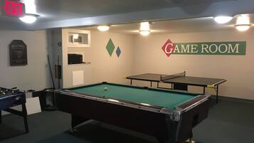 A pool table in a room with a billiards sign, a foosball table, and a table tennis table.