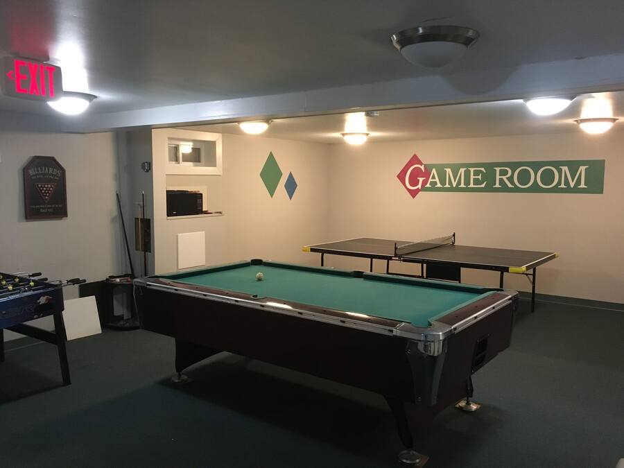 A pool table in a room with a billiards sign, a foosball table, and a table tennis table.