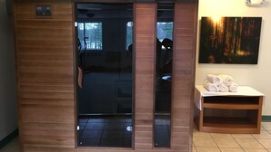 A sauna room with a wooden exterior, a glass door, and a bench with towels. - Highland Lake Resort (Bridgton)