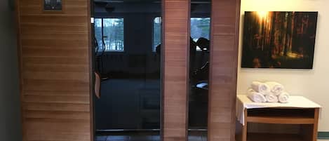A sauna room with a wooden exterior, a glass door, and a bench with towels.