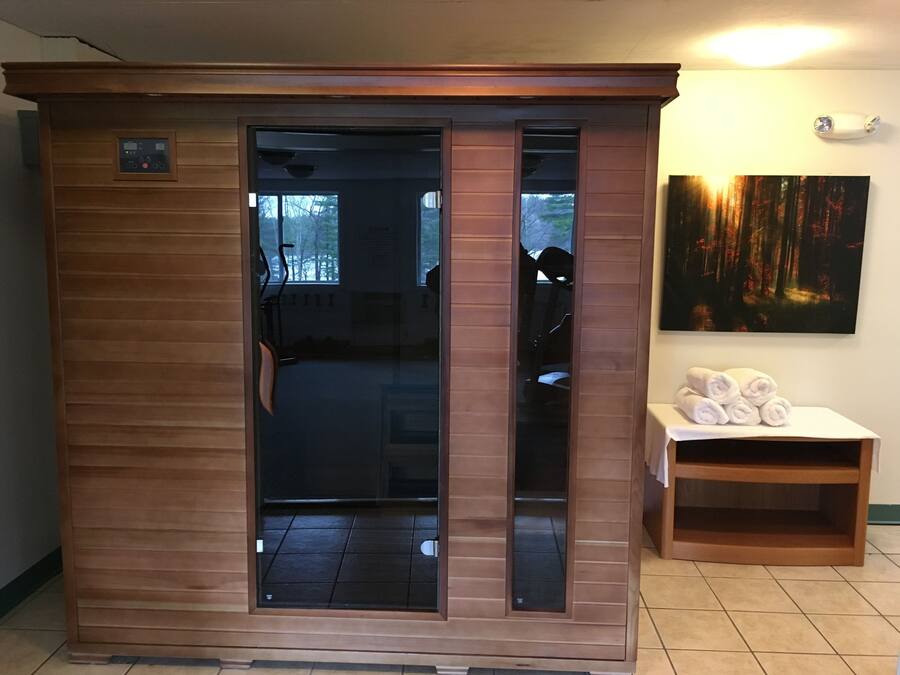A sauna room with a wooden exterior, a glass door, and a bench with towels.