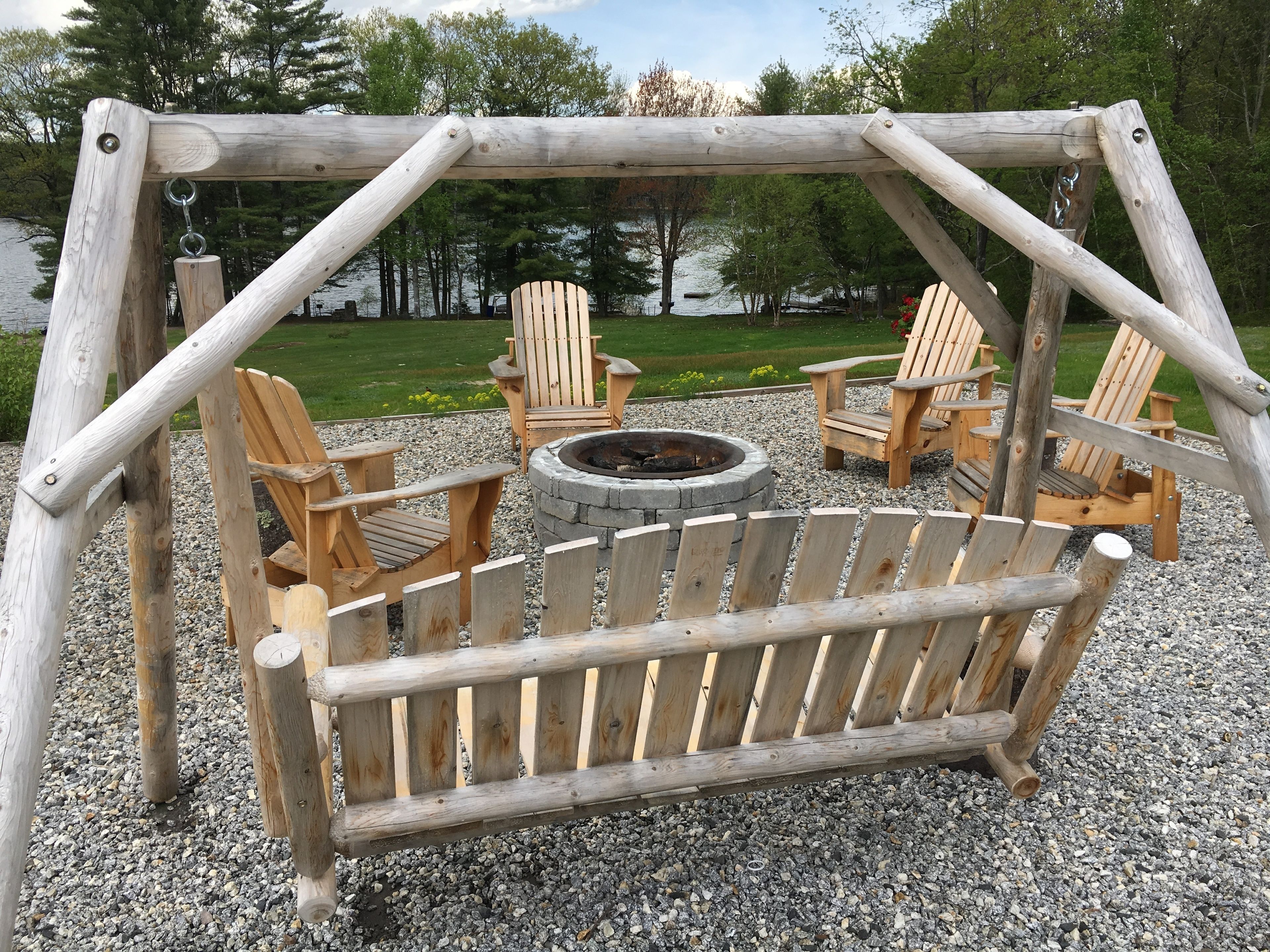 Ein Spielplatz mit Holzschaukel, Adirondack-Stühlen und einem Feuerkorb in einem Kiesbereich.