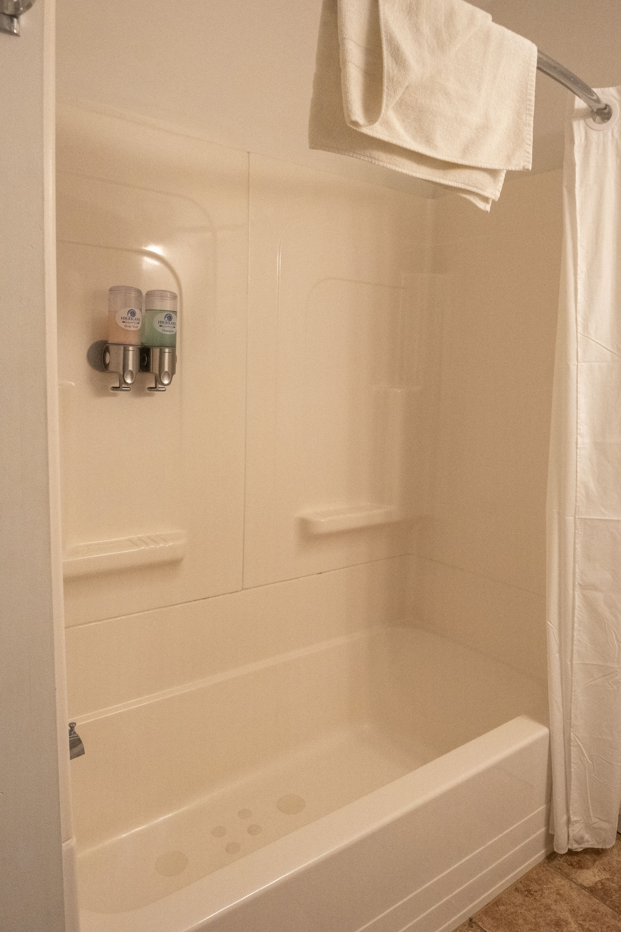 A white bathtub with a shower curtain, a towel rack, and two bottles of shampoo.