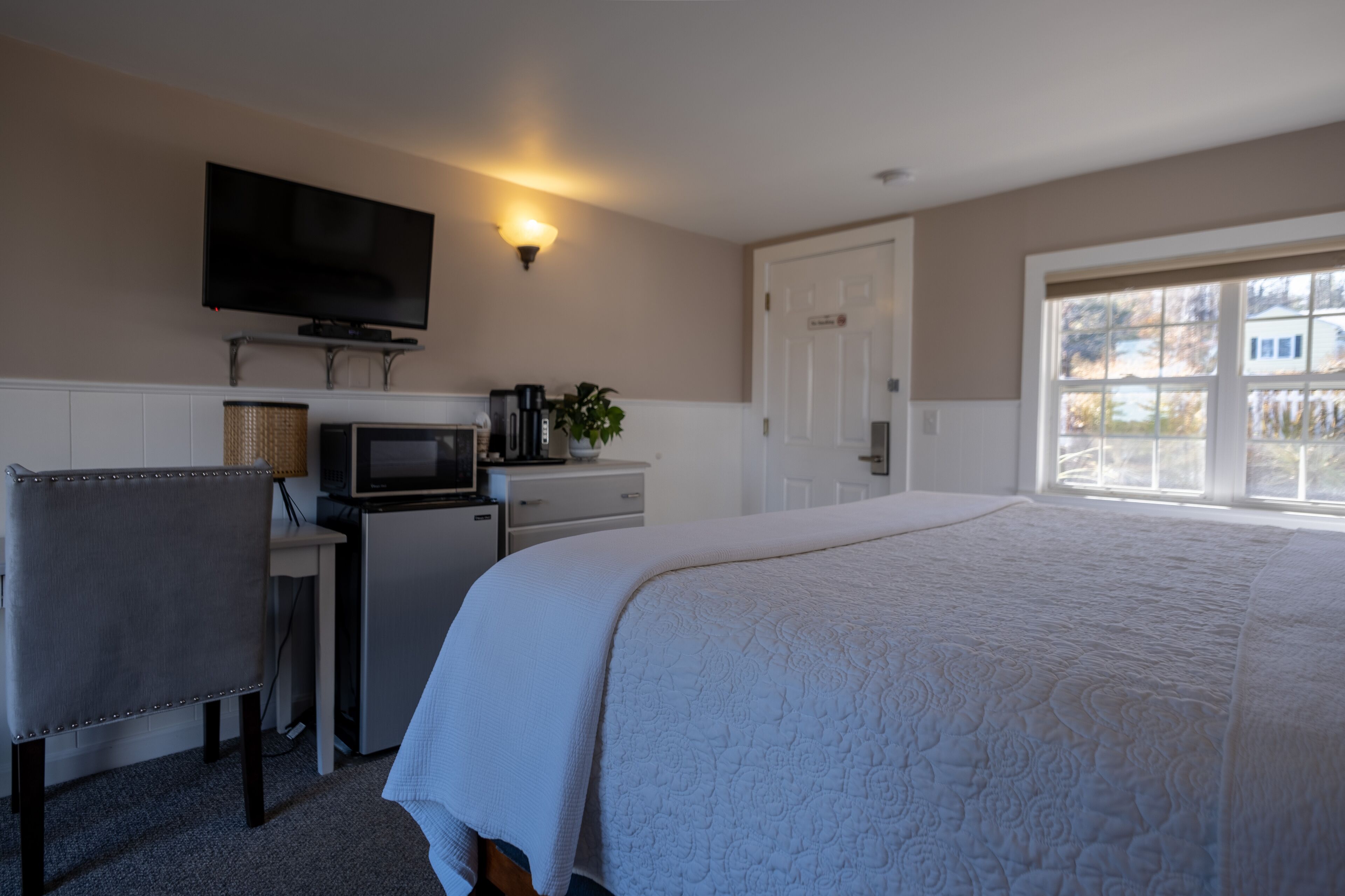 Una habitación de hotel con cama, escritorio, televisor, microondas y una pequeña cocina.