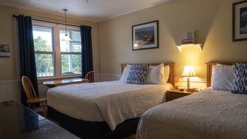 A hotel room with two beds, a desk, a chair, a window with curtains, a lamp, and a framed picture on the wall.