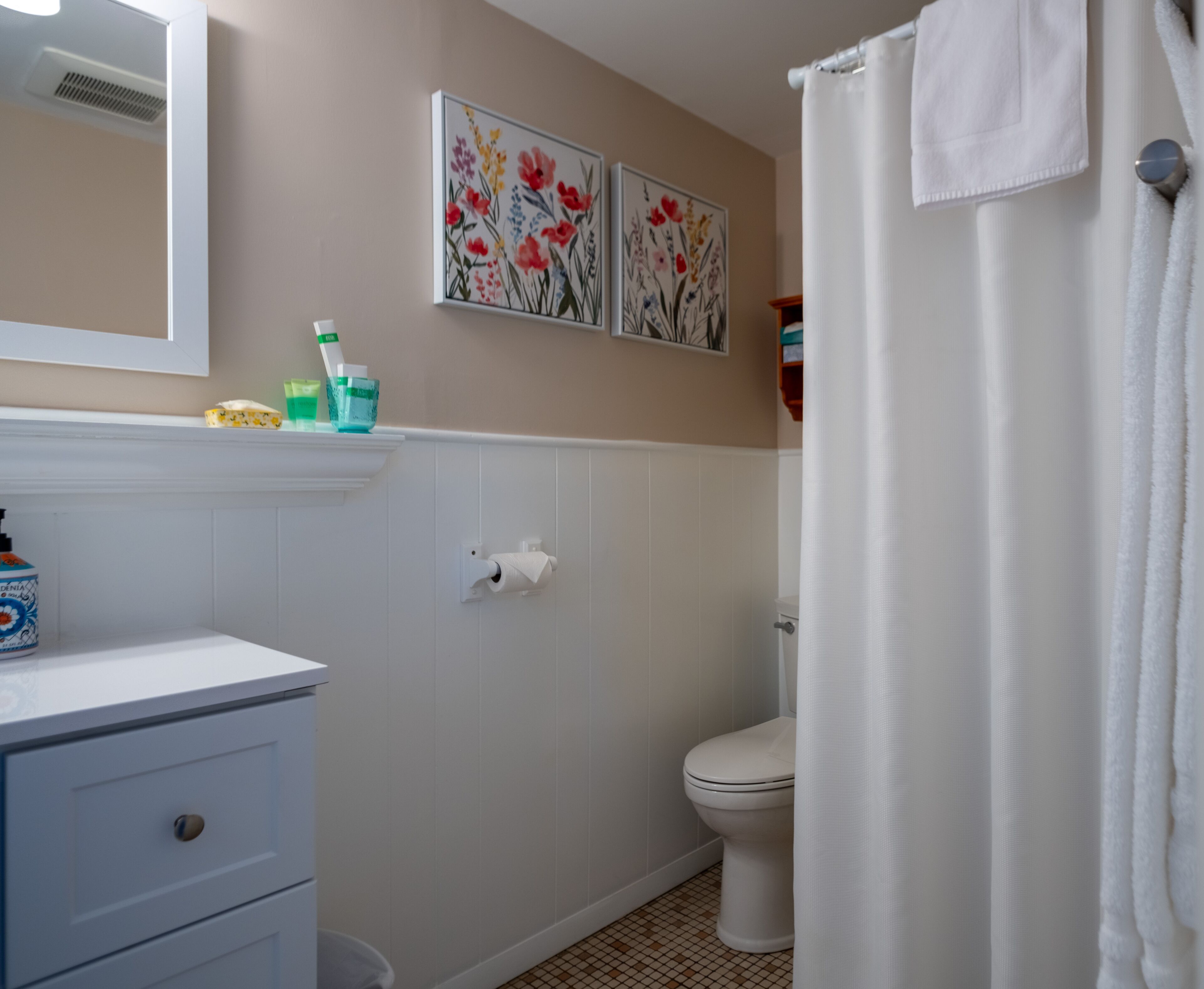 A bathroom with a toilet, a sink with a mirror, and two floral wall art pieces.
