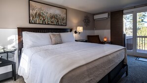 A large bed with a headboard, a bedside table, a lamp, and a painting on the wall. - Highland Lake Resort (Bridgton)