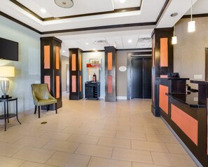 A hotel lobby with a reception desk, a chair, a small table with a lamp, and a fire extinguisher. - Hallmarc Studios (Port Arthur)