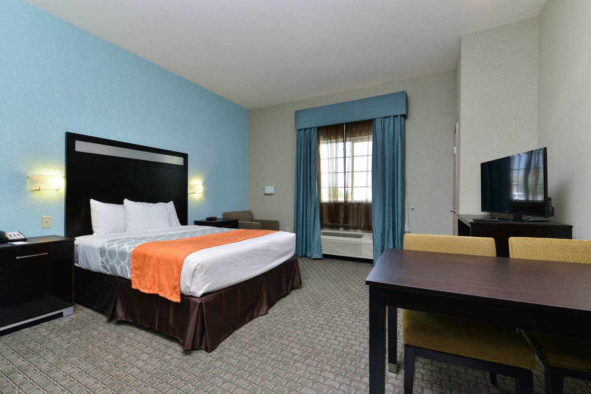 A hotel room with a bed, a desk, a television, and a window with curtains.