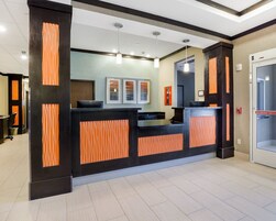 Un área de recepción con diseño en negro y naranja, un mostrador de recepción, cuadros en la pared y un detector de incendios.