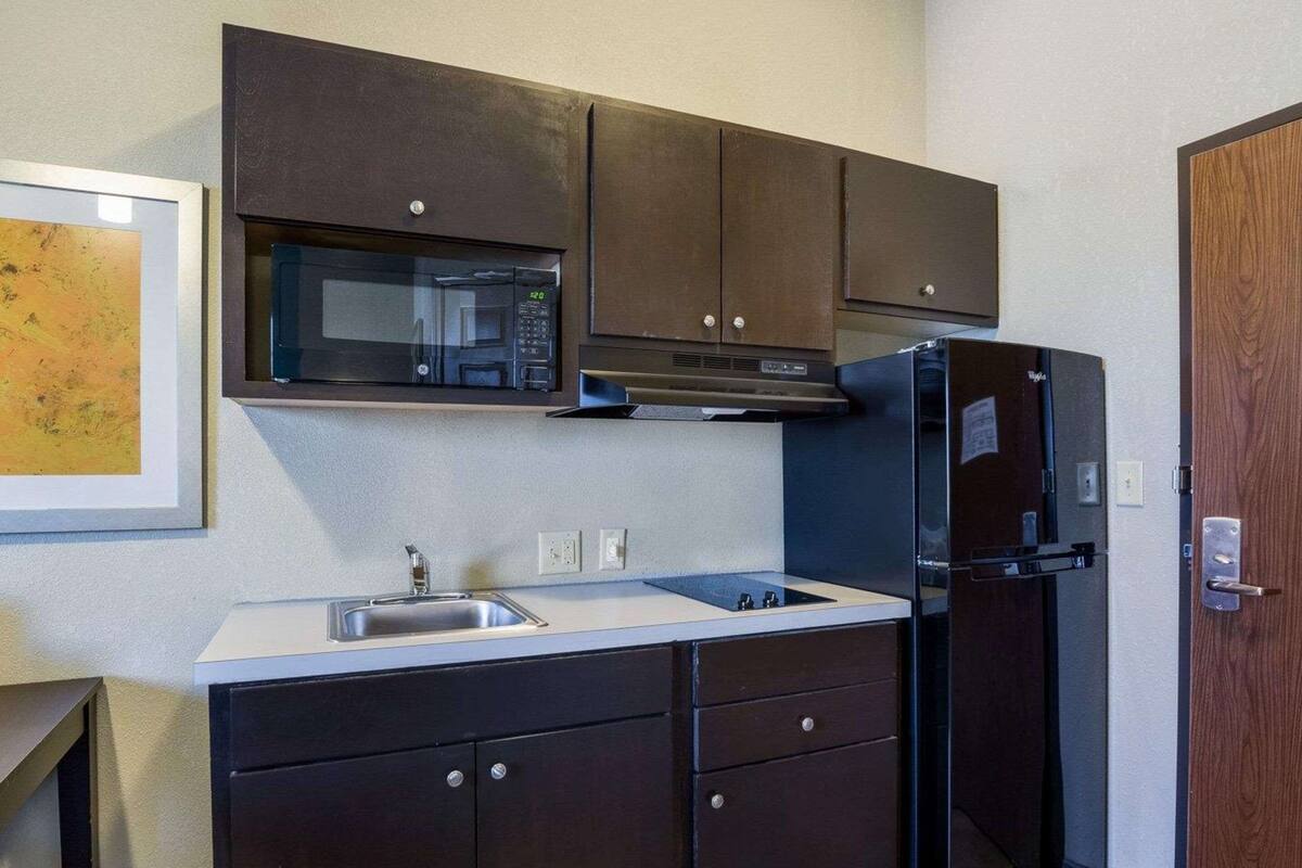 A compact kitchen with dark cabinets, a microwave, a refrigerator, and a sink.