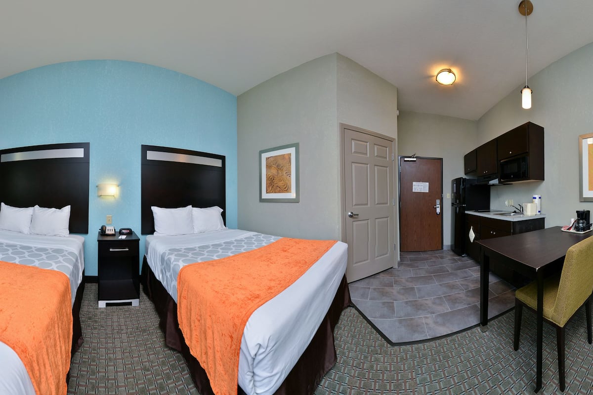 A hotel room with two beds, a desk, a TV, a microwave, and a dining area.