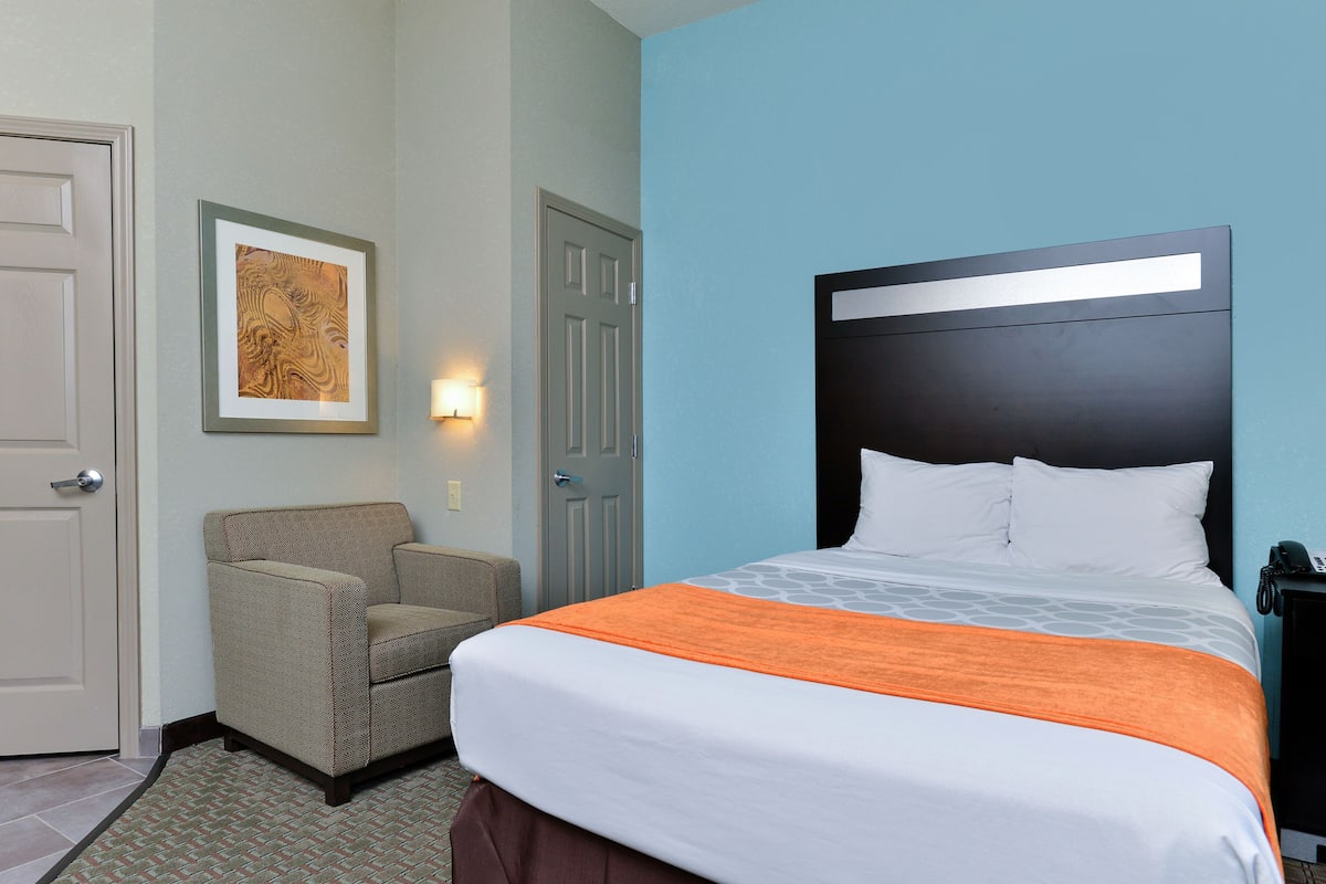 A hotel room with a bed, a chair, and a door.