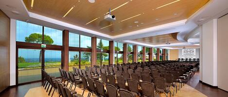 A conference room with rows of chairs, large windows with a view, and a wooden ceiling with recessed lighting.