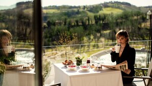 A table set with breakfast items, a book, and a glass of drink, overlooking a scenic landscape. - Palazzo di Varignana Resort & SPA (Castel San Pietro Terme)