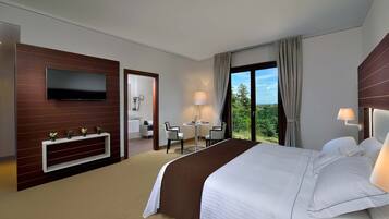 Habitación de hotel con una cama grande, un televisor montado en la pared, un escritorio con sillas y vistas al exterior.
