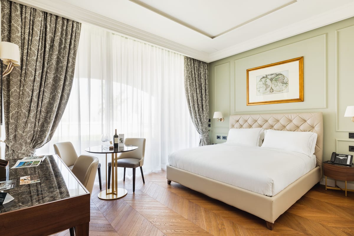 Ein Hotelzimmer mit einem großen Bett, einem Schreibtisch mit Stühlen, einem runden Tisch und einem gerahmten Bild an der Wand.